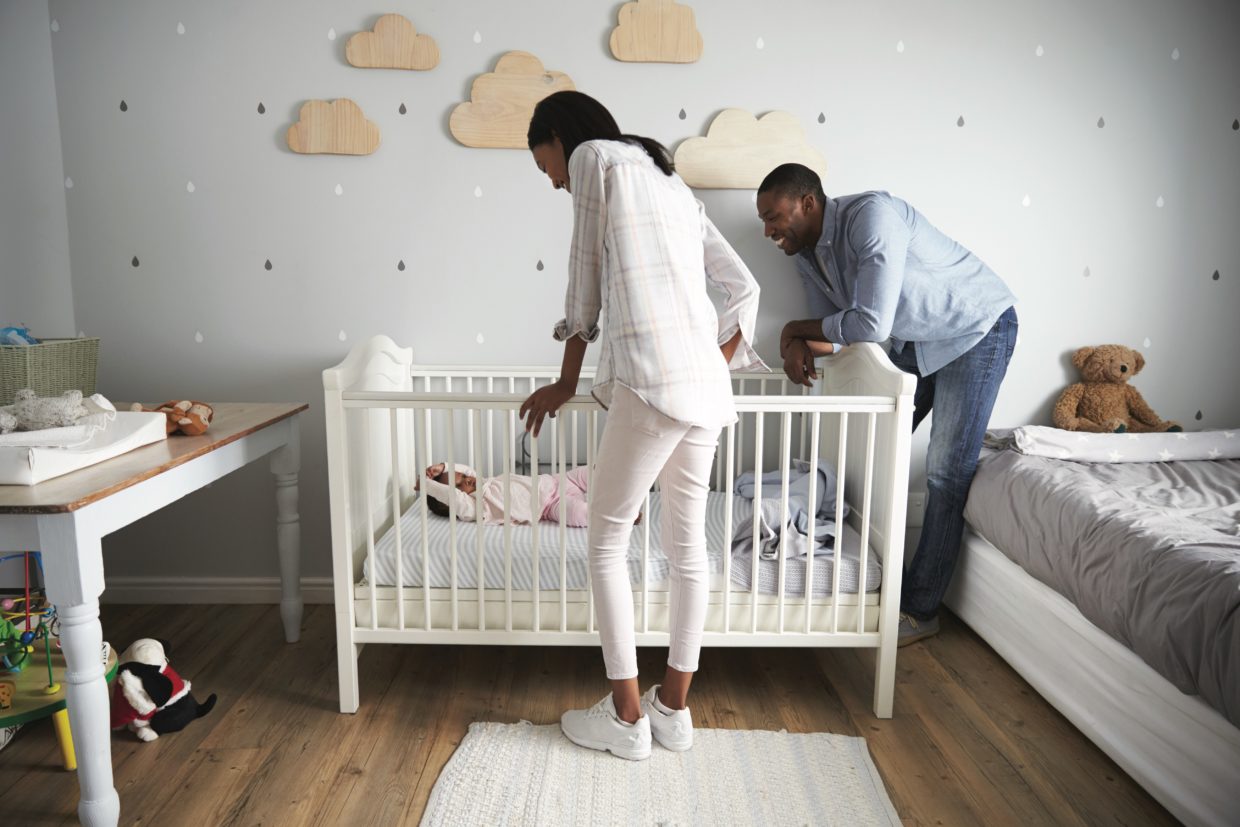 Mother And Father Looking At Baby Daughter In Nursery Cot